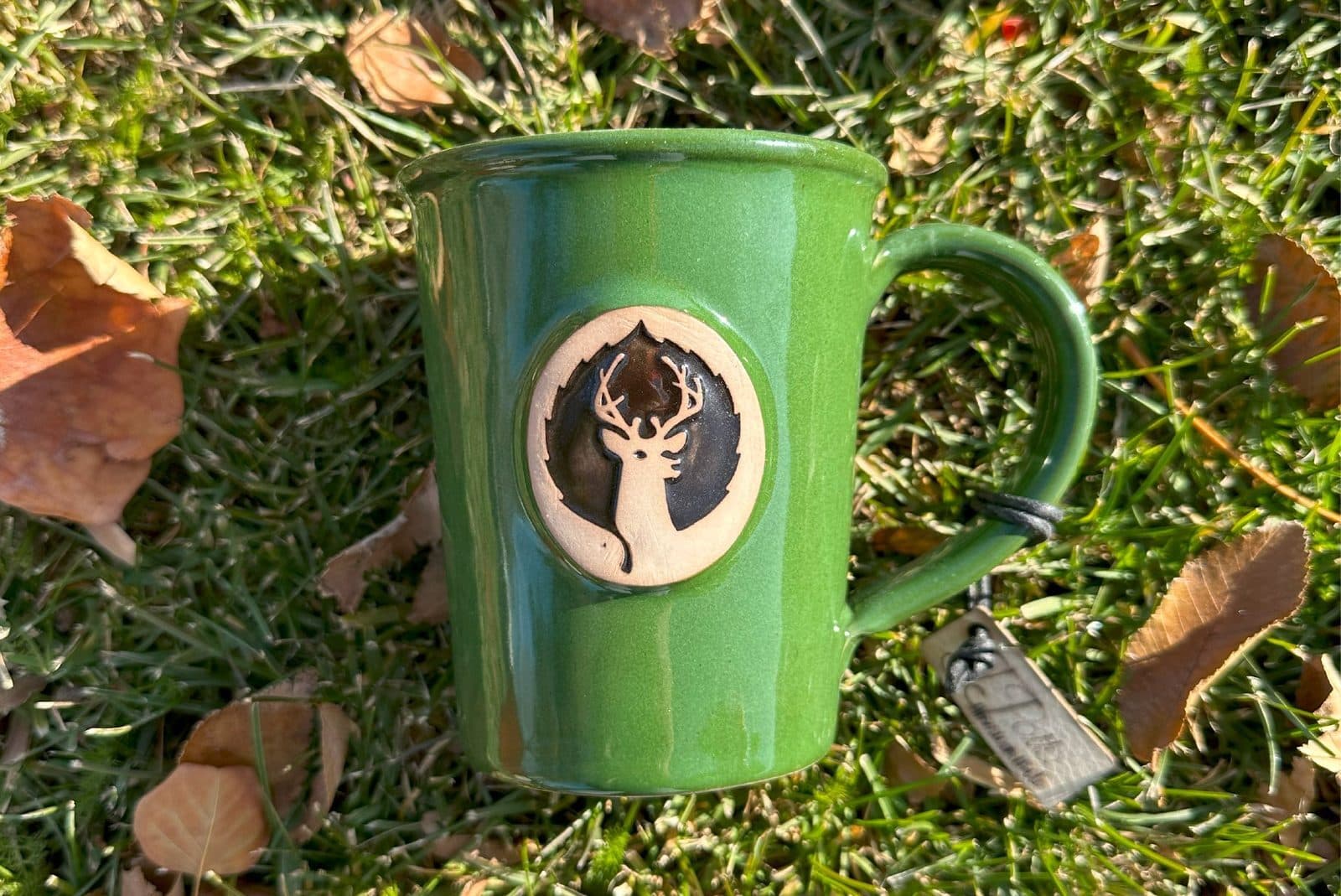 Deer-logo green ceramic mug on autumn leaves