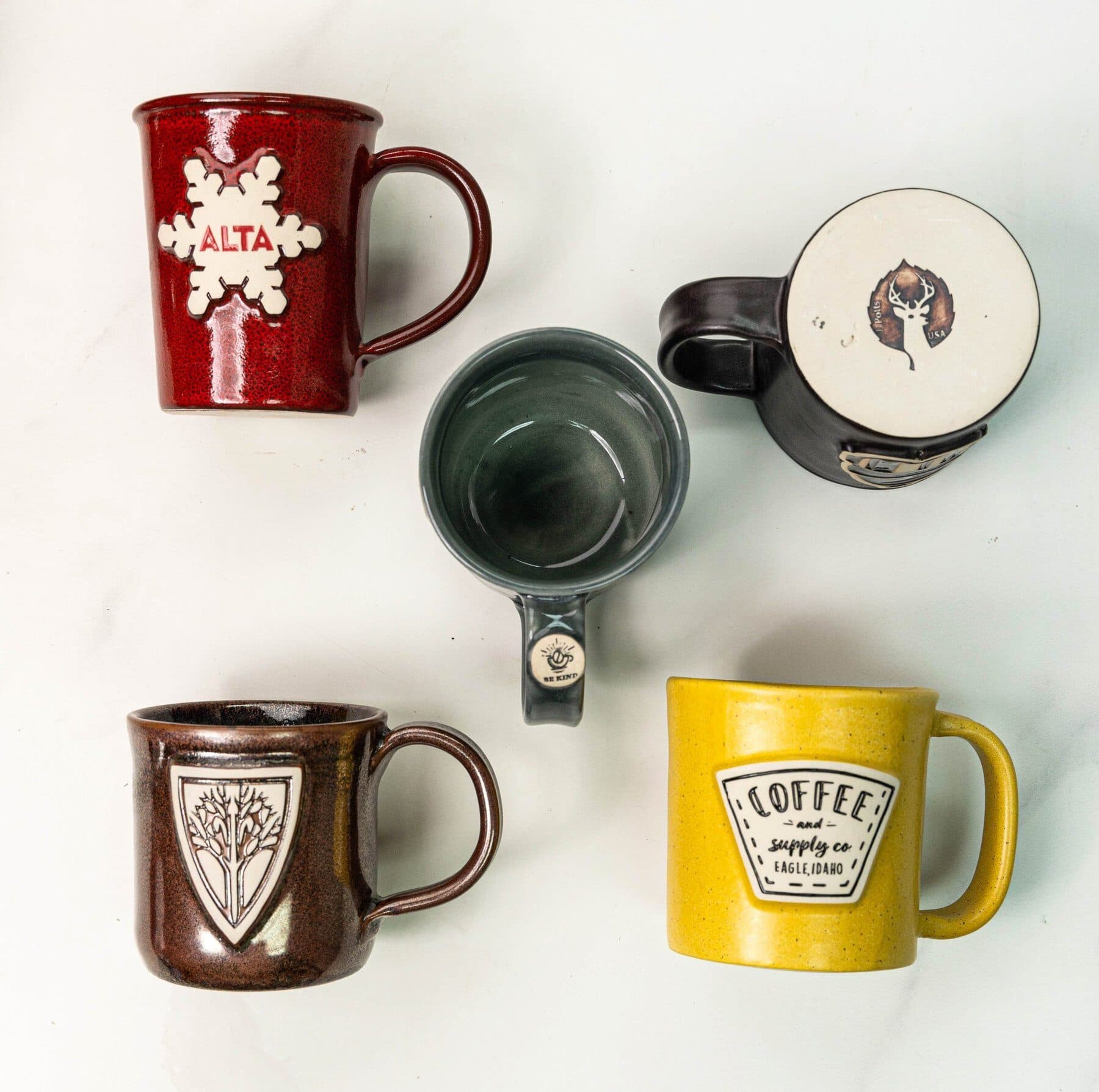 An overhead arrangement of custom JJ Potts mugs in different glazes and logos