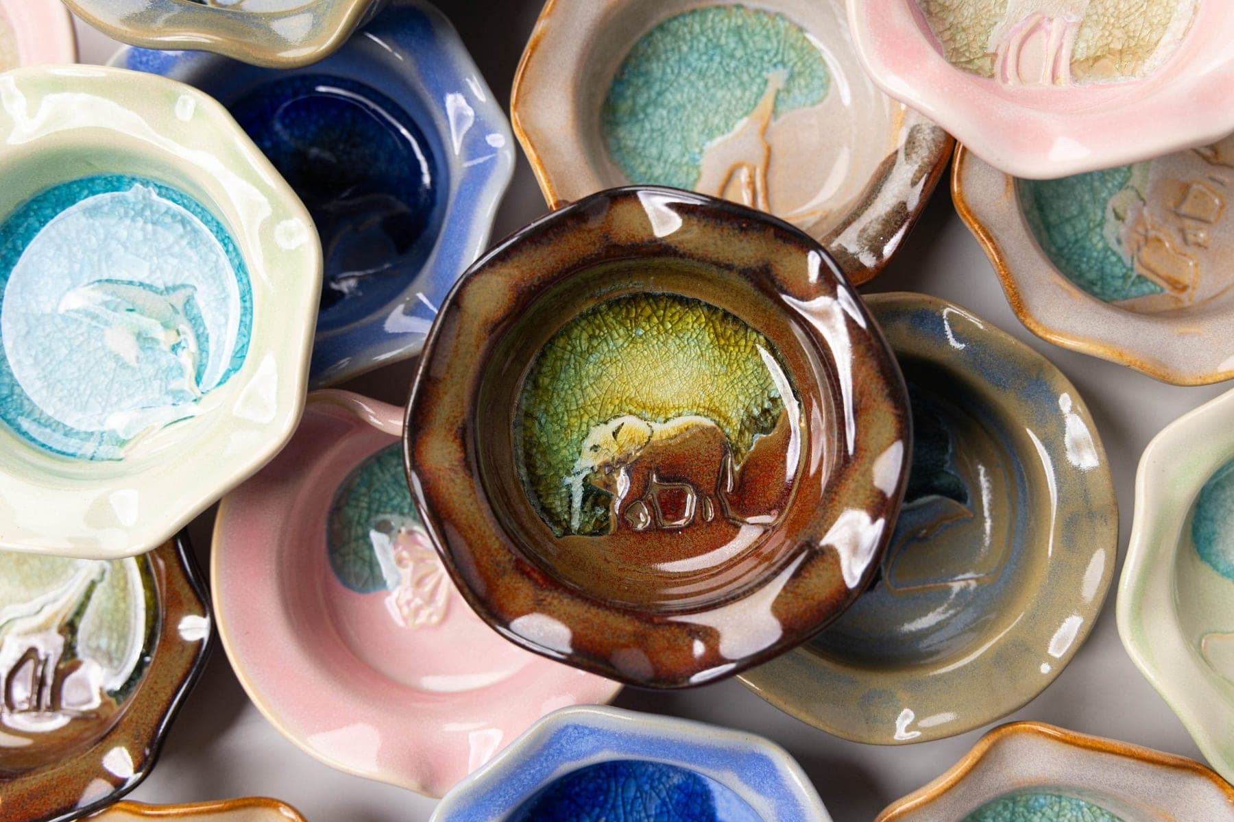 A close assortment of trinket dishes in pink, teal, cream, and brown glazes with animal and nature stamps