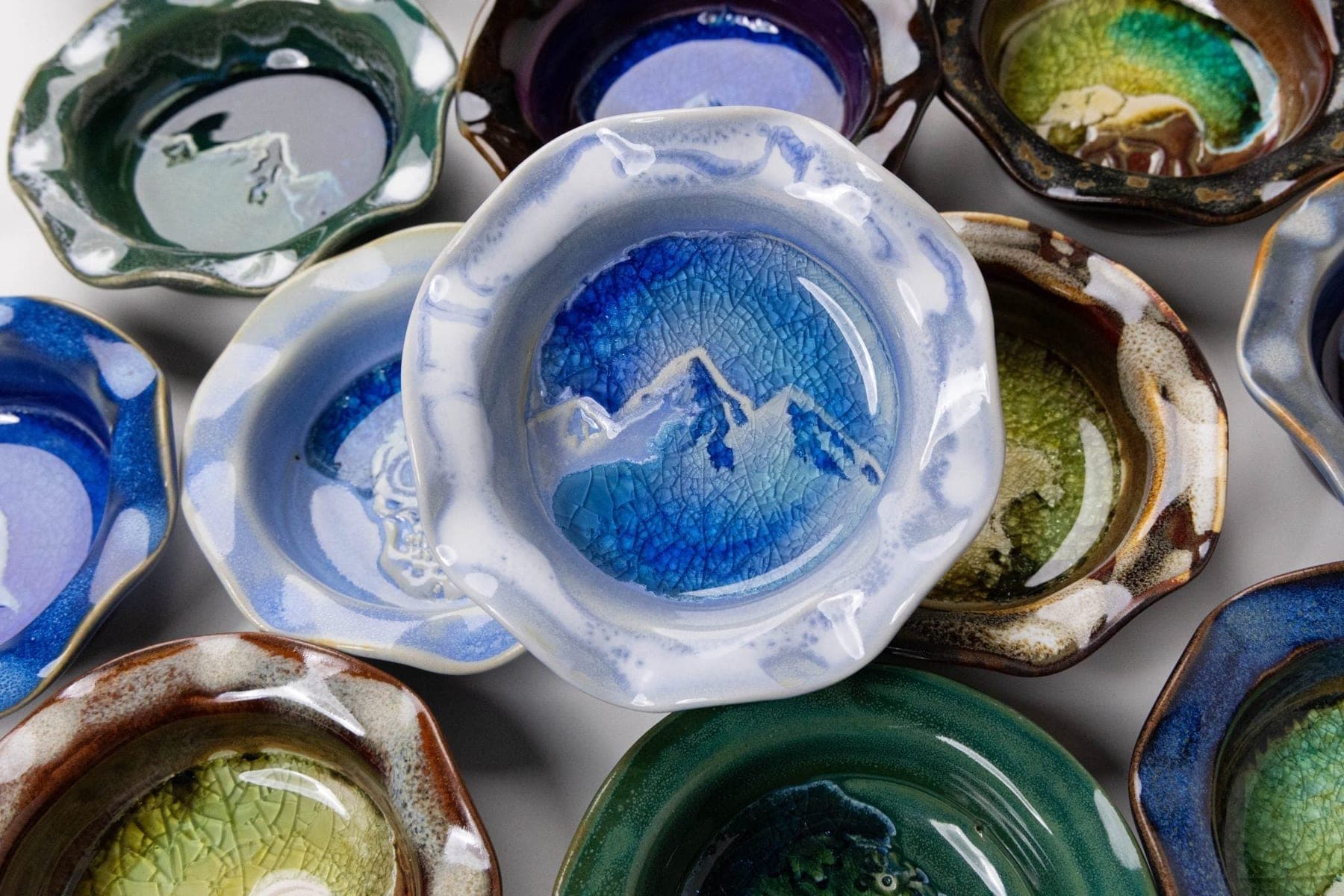 Trinket dishes stamped with mountain, elephant, and leaf designs in blue, green, and amber glazes